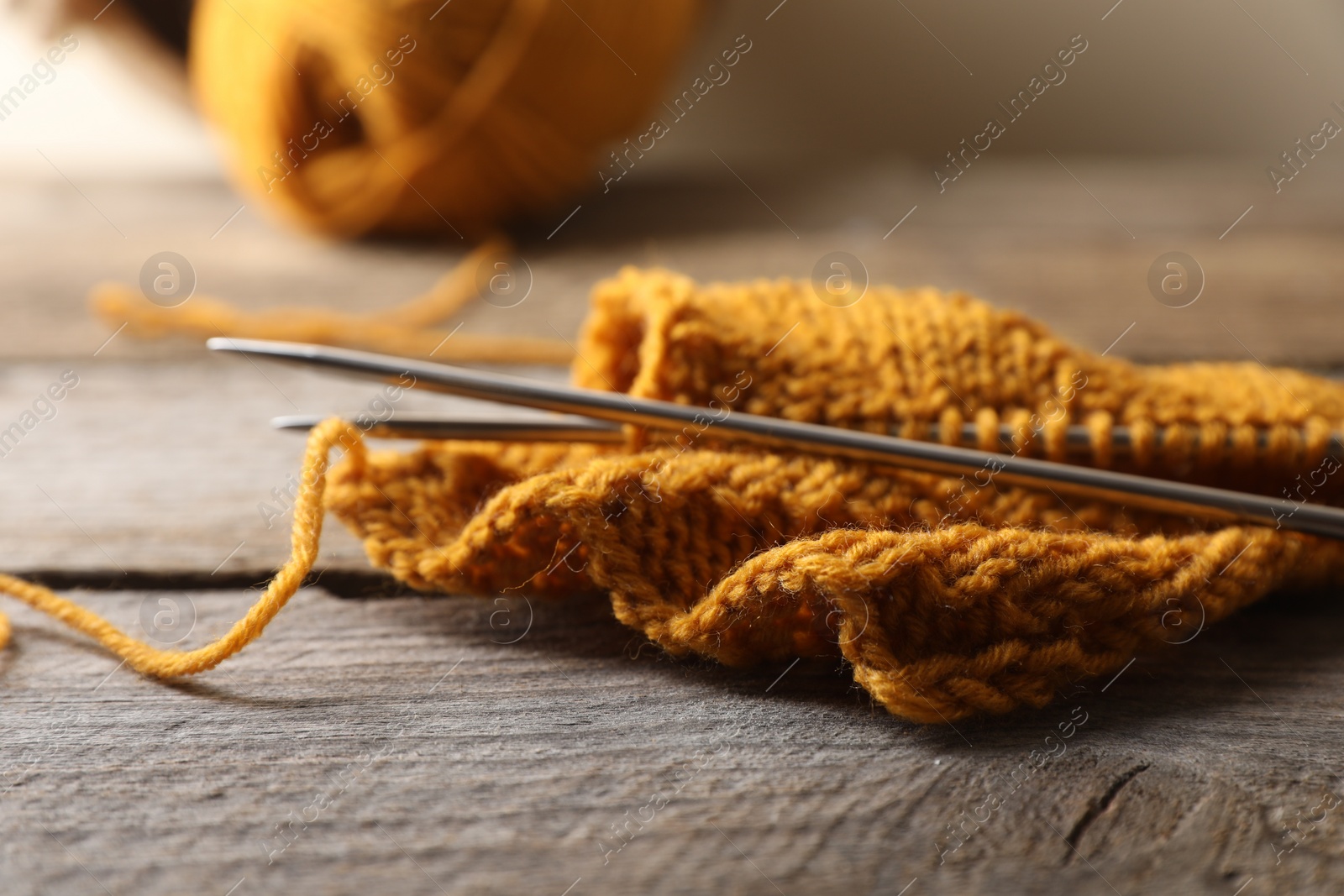 Photo of Soft orange knitting and metal needles on wooden table, closeup