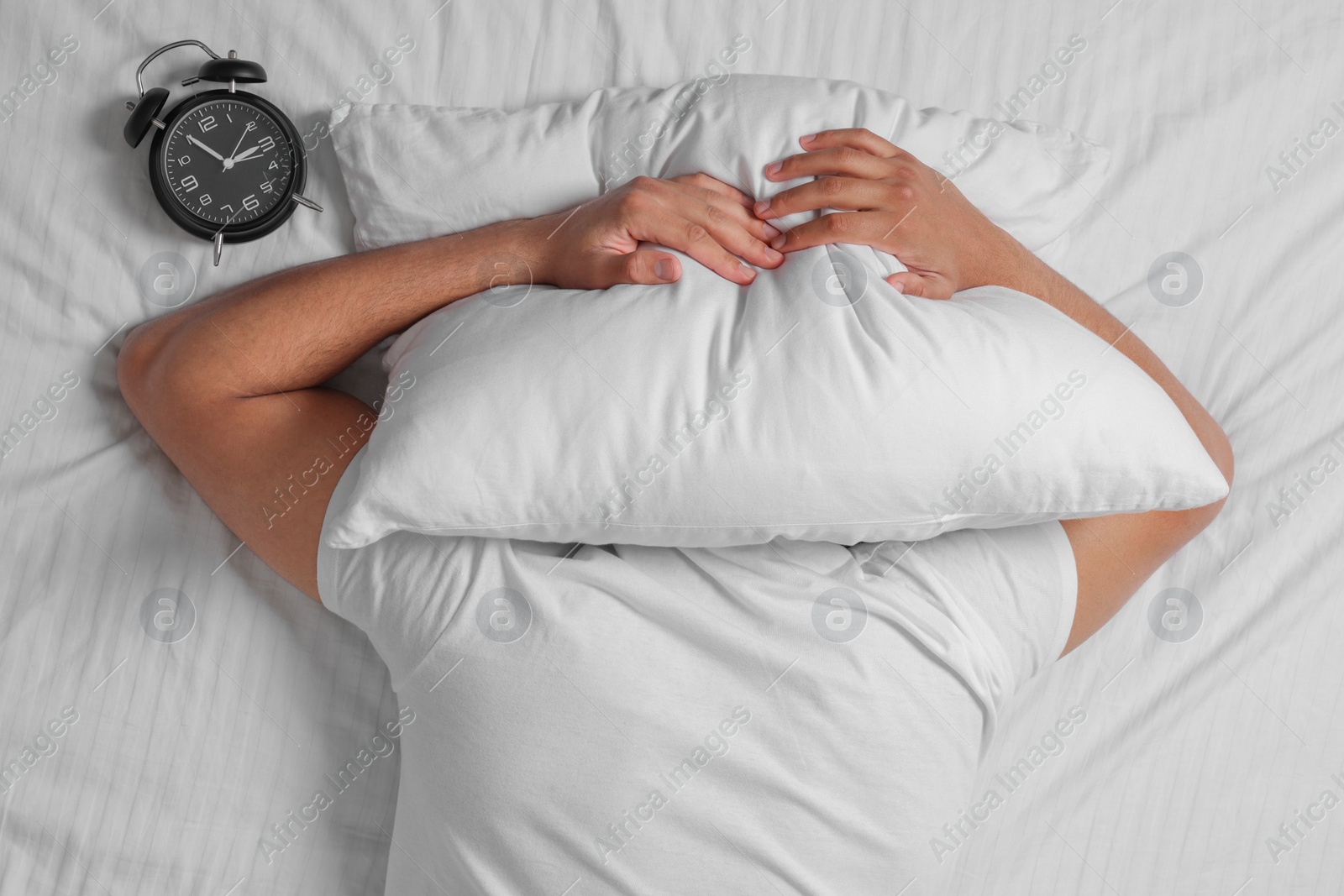 Photo of Man suffering from insomnia near alarm clock on bed, top view