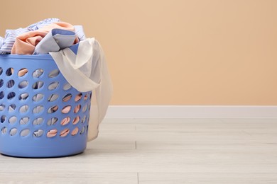 Photo of Laundry basket with clothes near beige wall indoors. Space for text