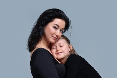 Photo of Beautiful mother hugging with little daughter on grey background