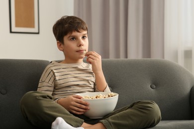 Photo of Little boy eating popcorn while watching TV at home