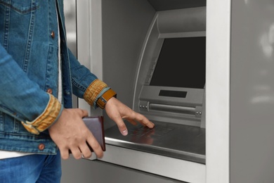 Photo of Man entering PIN code on cash machine keypad outdoors, closeup