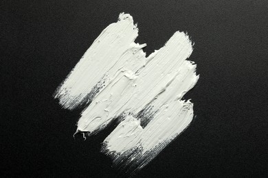 Photo of Strokes of white oil paint on black canvas, top view