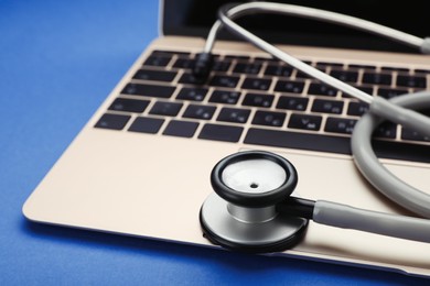 Photo of Laptop with stethoscope on blue background, closeup