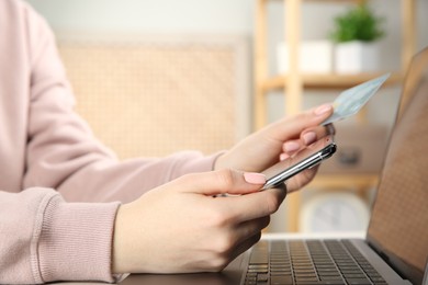 Photo of Online payment. Woman using credit card and smartphone near laptop indoors, closeup