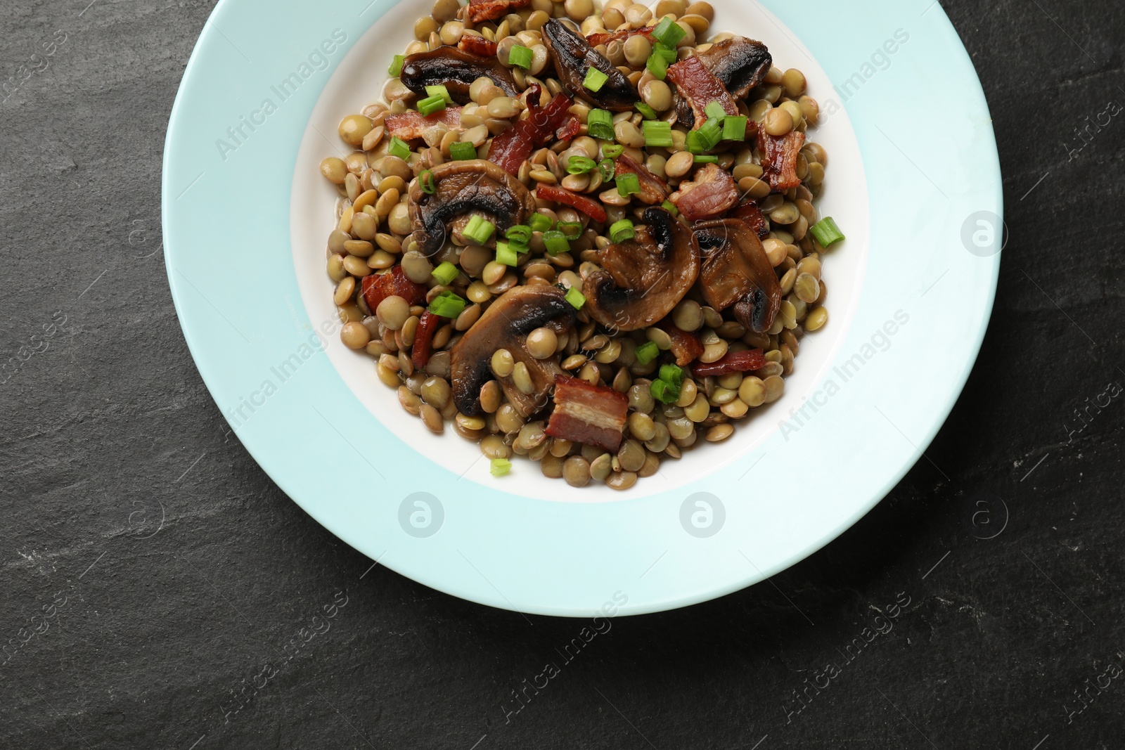 Photo of Delicious lentils with mushrooms, bacon and green onion on grey textured table, top view