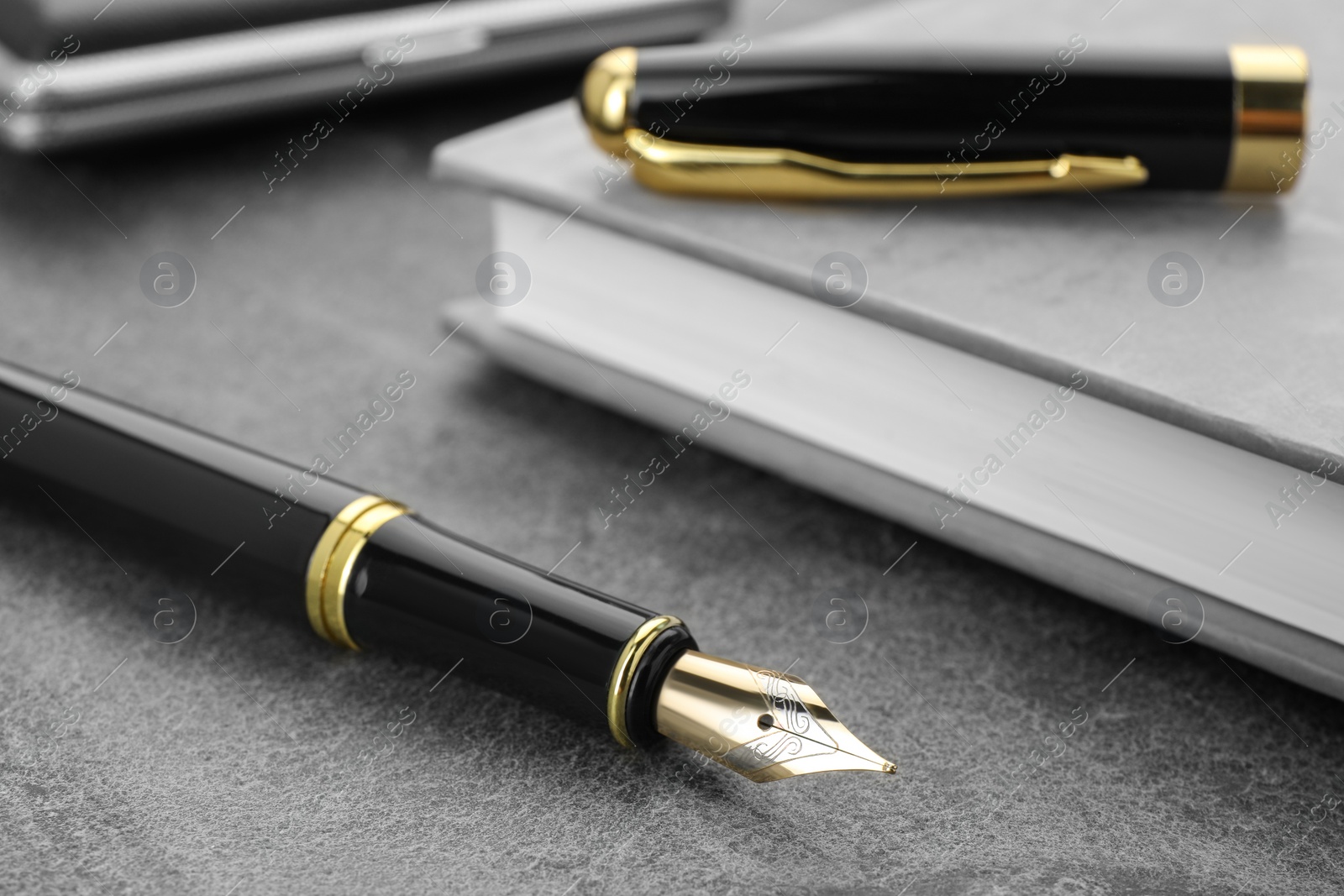 Photo of Stylish black fountain pen and notebook on grey textured table, closeup