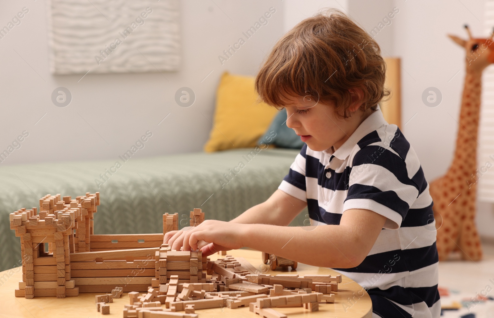 Photo of Cute little boy playing with wooden construction set at table in room. Child's toy