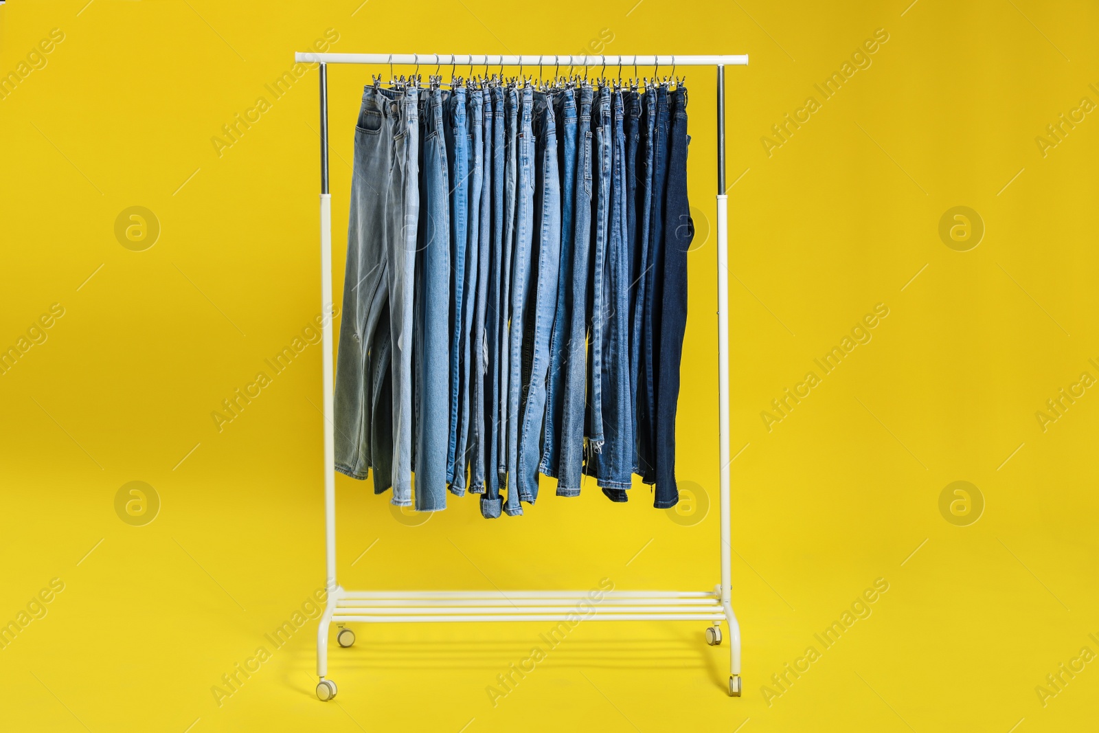 Photo of Rack with different jeans on yellow background