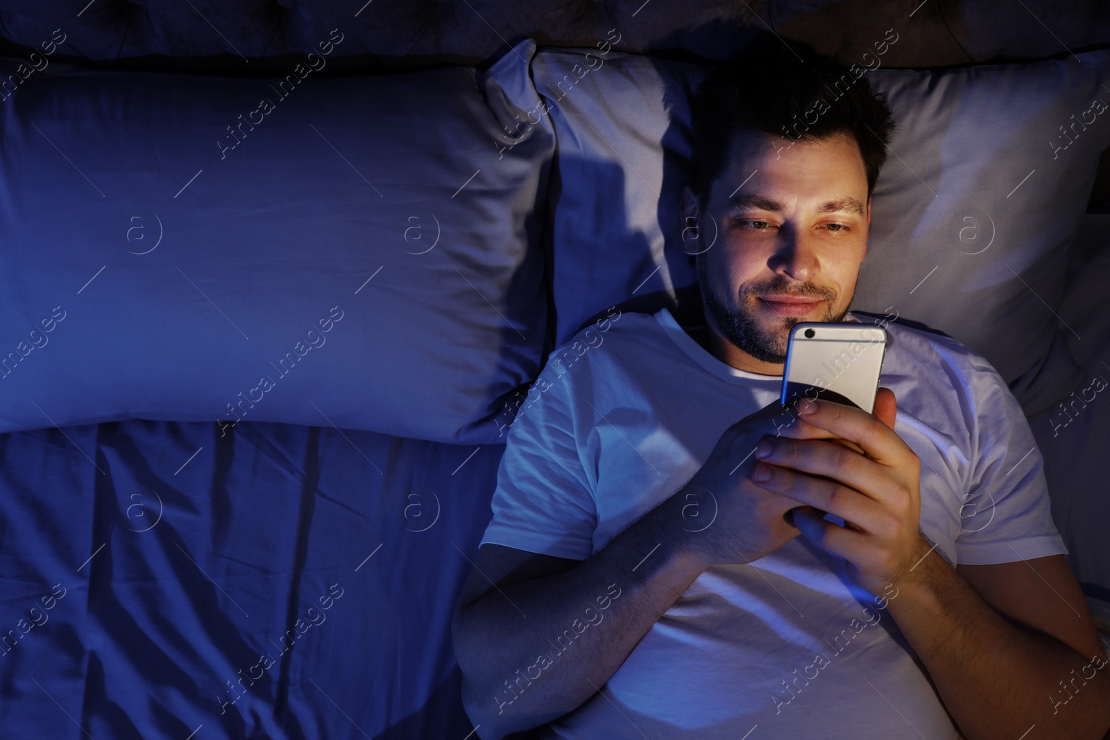 Photo of Handsome man using smartphone at night, space for text. Bedtime