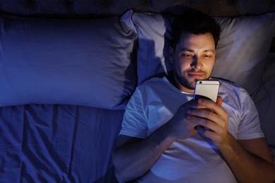 Photo of Handsome man using smartphone at night, space for text. Bedtime