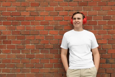 Handsome young man with headphones near red brick wall. Space for text