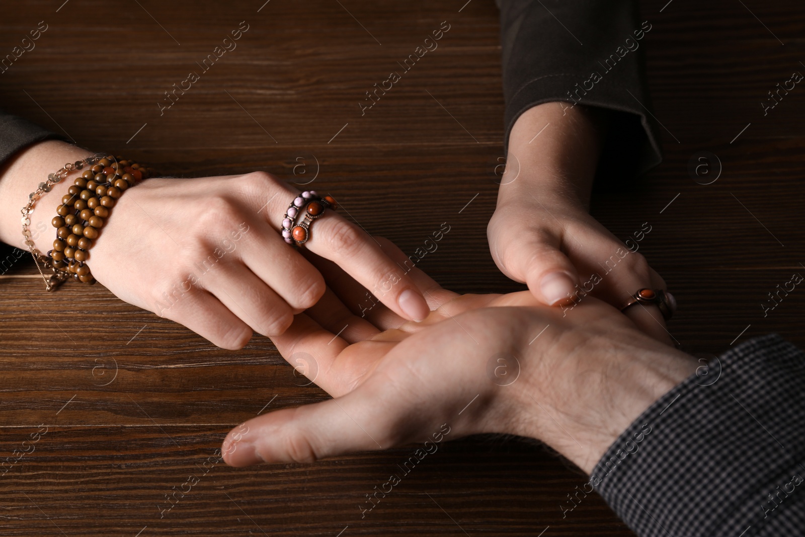 Photo of Chiromancer reading lines on man's palm at table, closeup