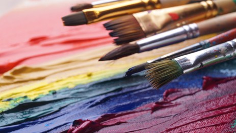 Photo of Many brushes on artist's palette with colorful mixed paints, closeup