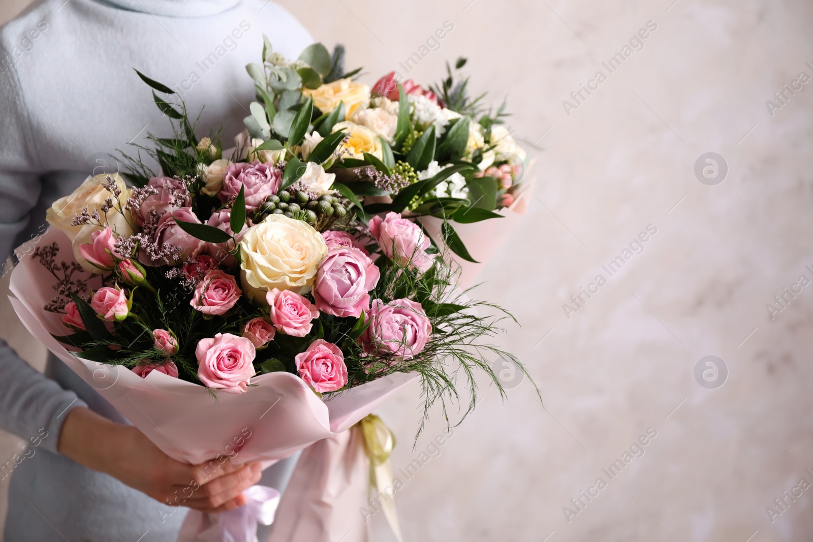 Photo of Woman with bouquets of beautiful flowers on beige background, closeup. Space for text