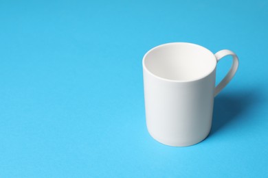 Photo of One white ceramic mug on light blue background, space for text