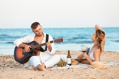 Photo of Young couple with guitar having romantic dinner on beach