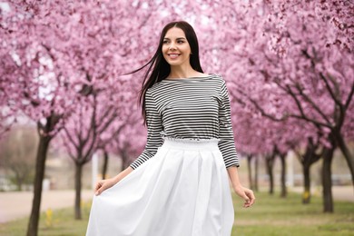 Pretty young woman in park with blooming trees. Spring look