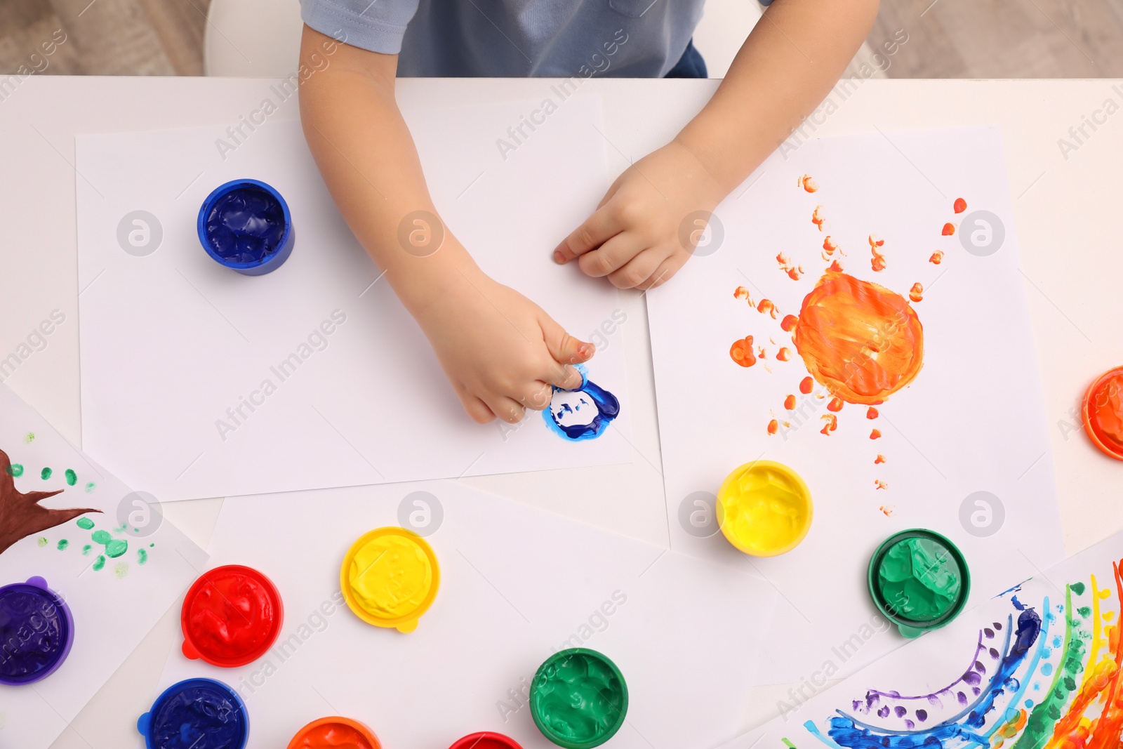 Photo of Little child painting with finger at white table indoors, top view