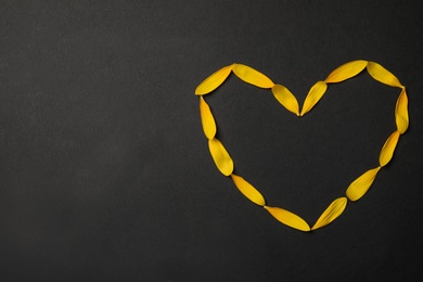 Photo of Heart shaped frame made with yellow sunflower petals on black background, flat lay. Space for text