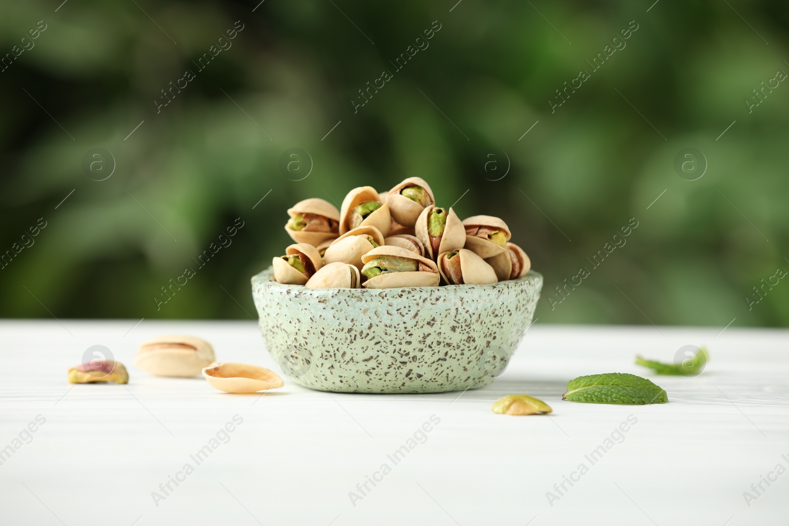 Photo of Tasty pistachios in bowl on white table against blurred background