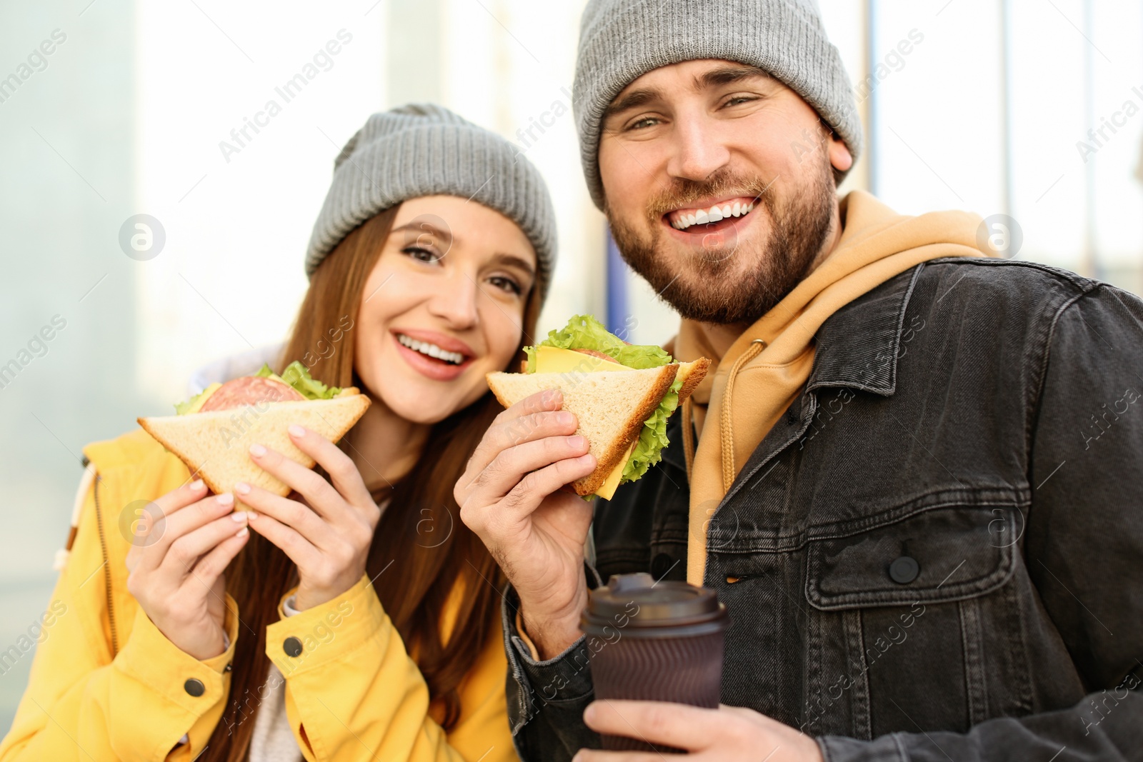 Photo of Happy young couple with sandwiches and coffee on city street