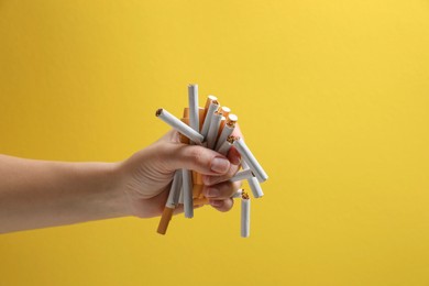 Photo of Stop smoking. Woman holding whole and broken cigarettes on yellow background, closeup. Space for text