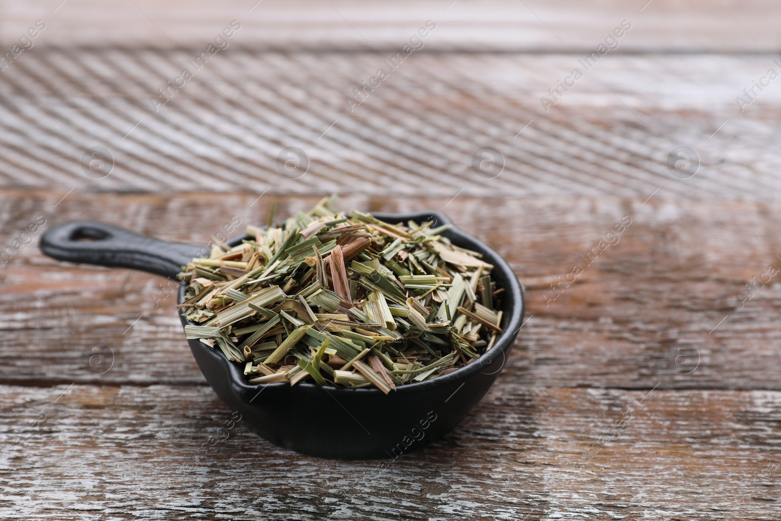 Photo of Small saucepan with aromatic dried lemongrass on wooden table. Space for text