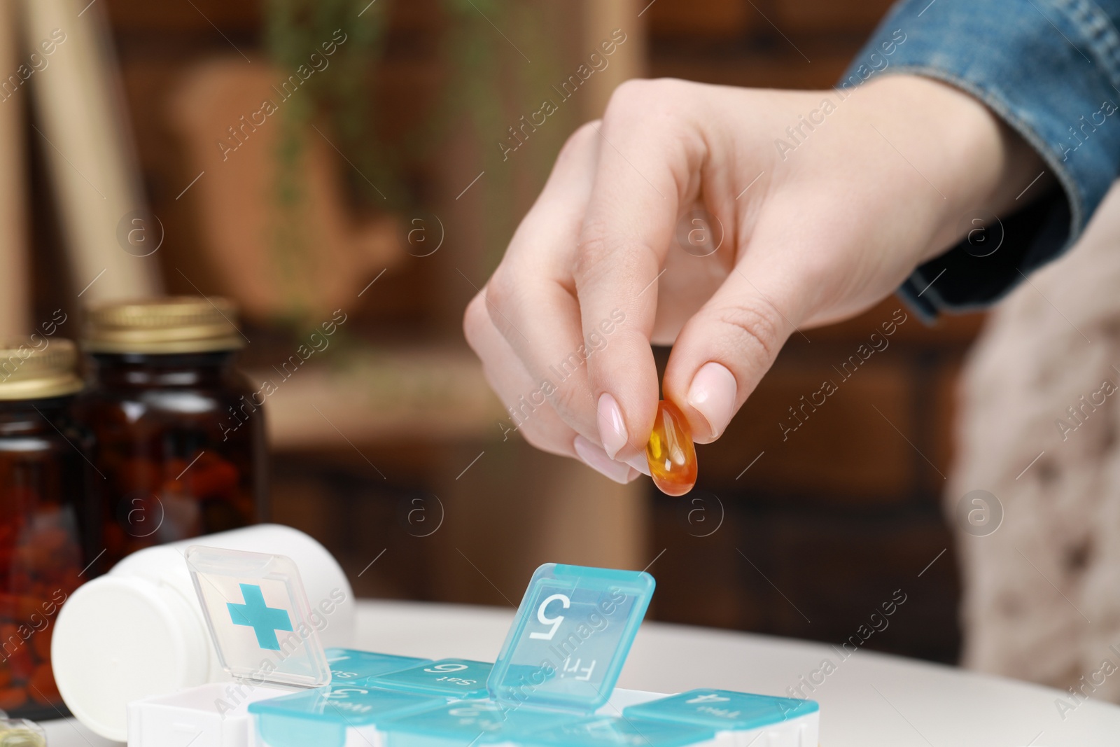 Photo of Woman taking pill from plastic container at white table indoors, closeup