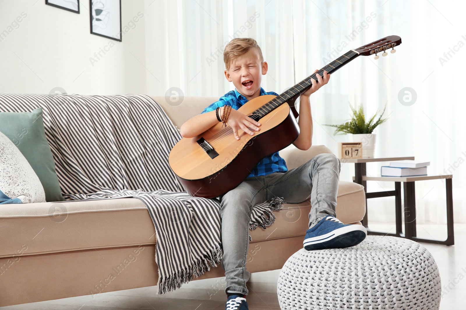 Photo of Cute little boy playing guitar on sofa in room