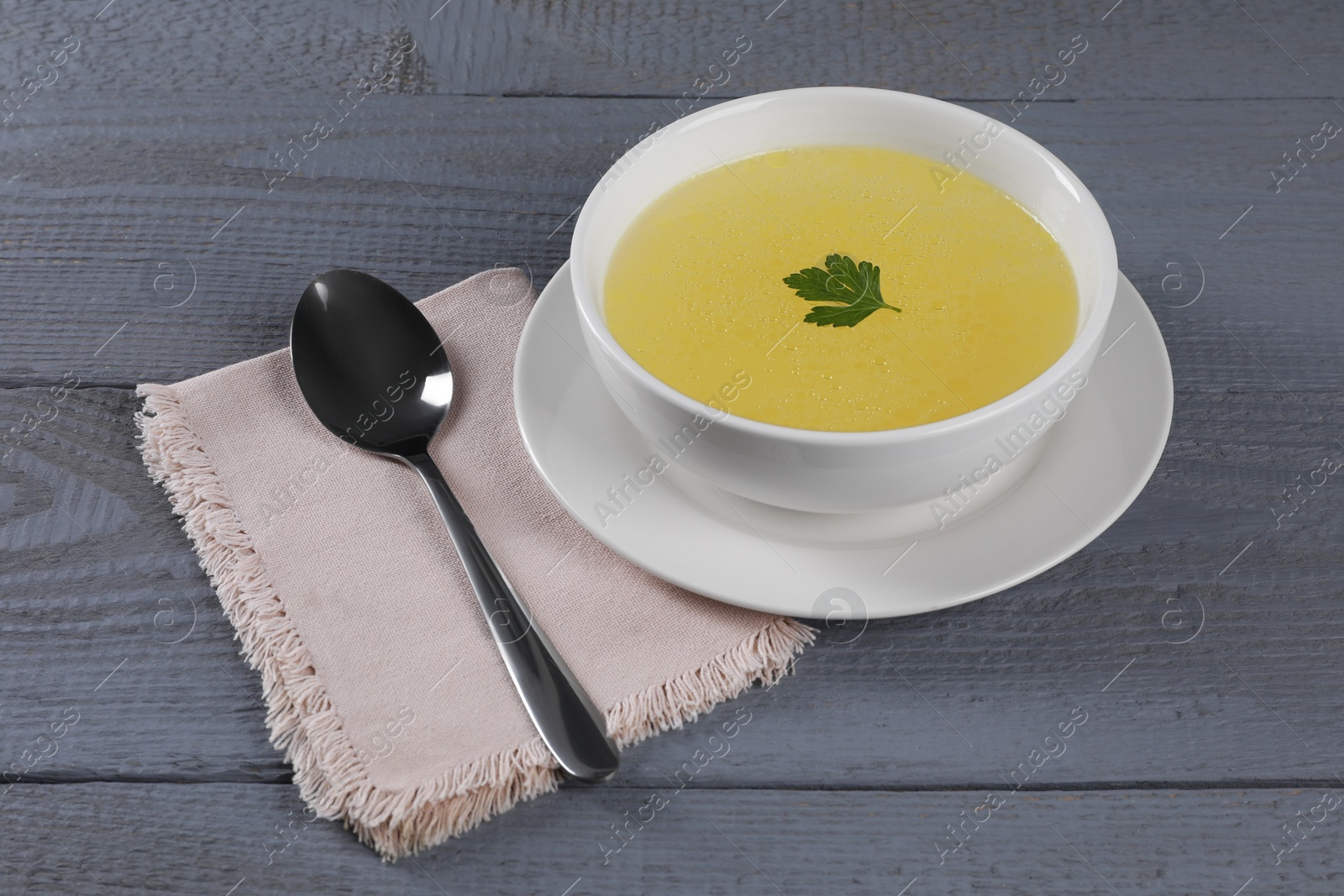 Photo of Tasty broth in bowl on grey wooden table