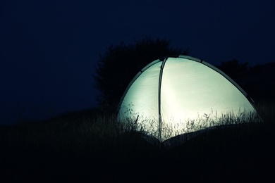 Photo of Small camping tent glowing in twilight outdoors. Space for text