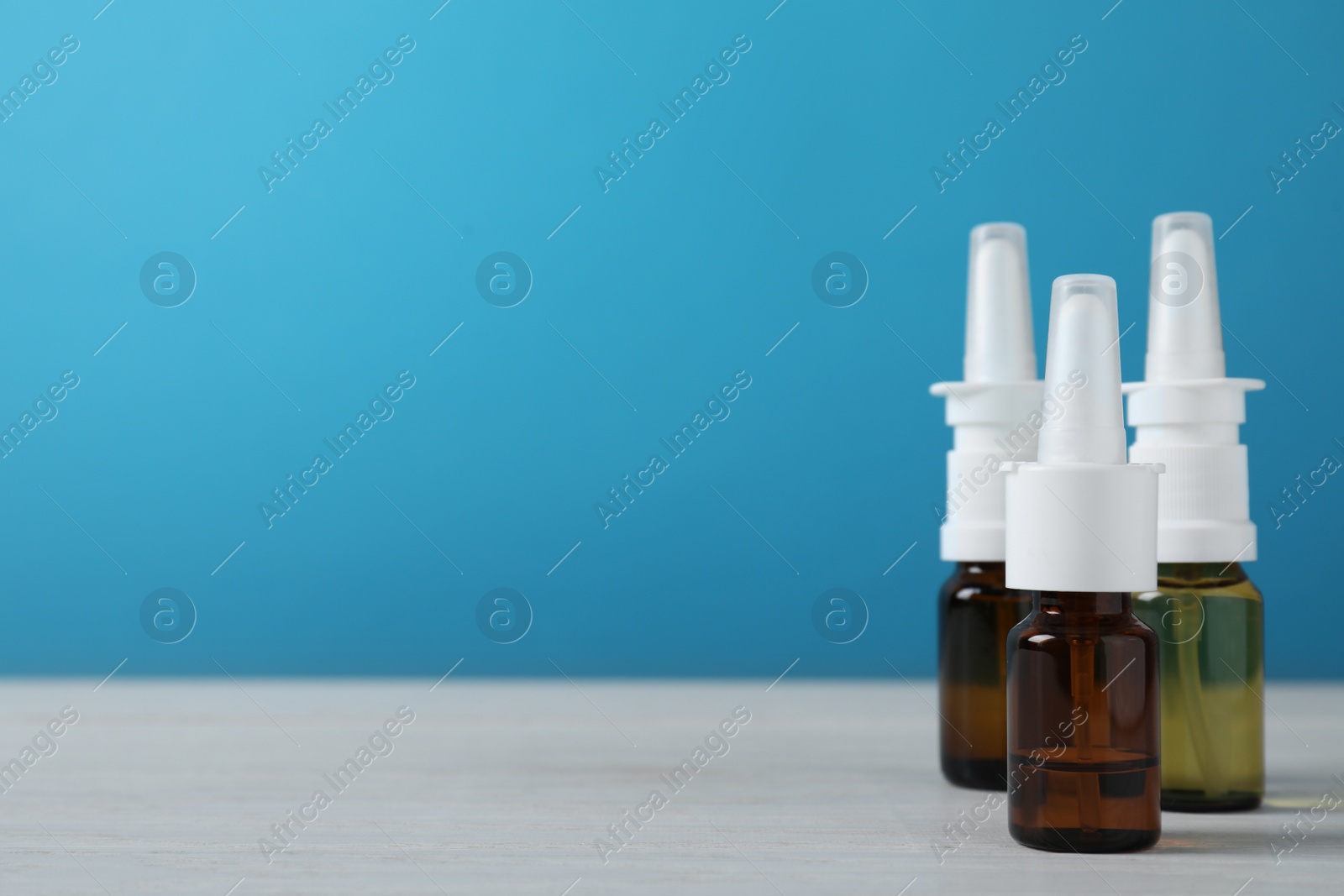 Photo of Bottles of nasal sprays on white wooden table. Space for text