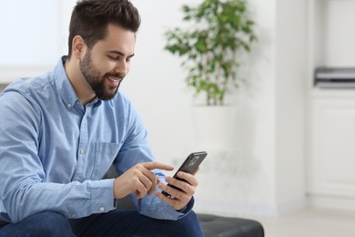 Handsome young man using smartphone in office, space for text