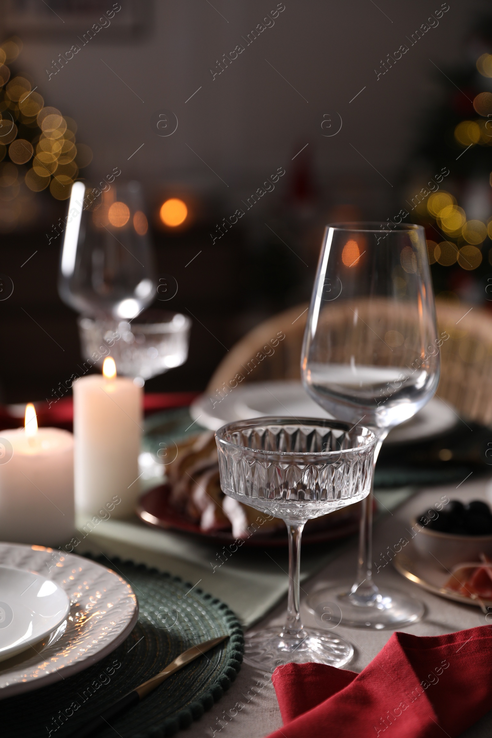 Photo of Christmas table setting with burning candles, appetizers and dishware indoors, closeup