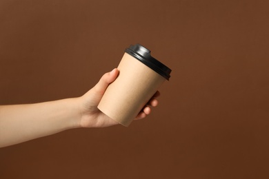 Woman holding takeaway paper coffee cup on brown background, closeup
