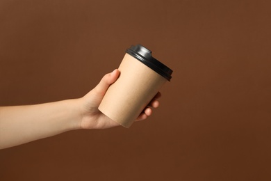 Photo of Woman holding takeaway paper coffee cup on brown background, closeup