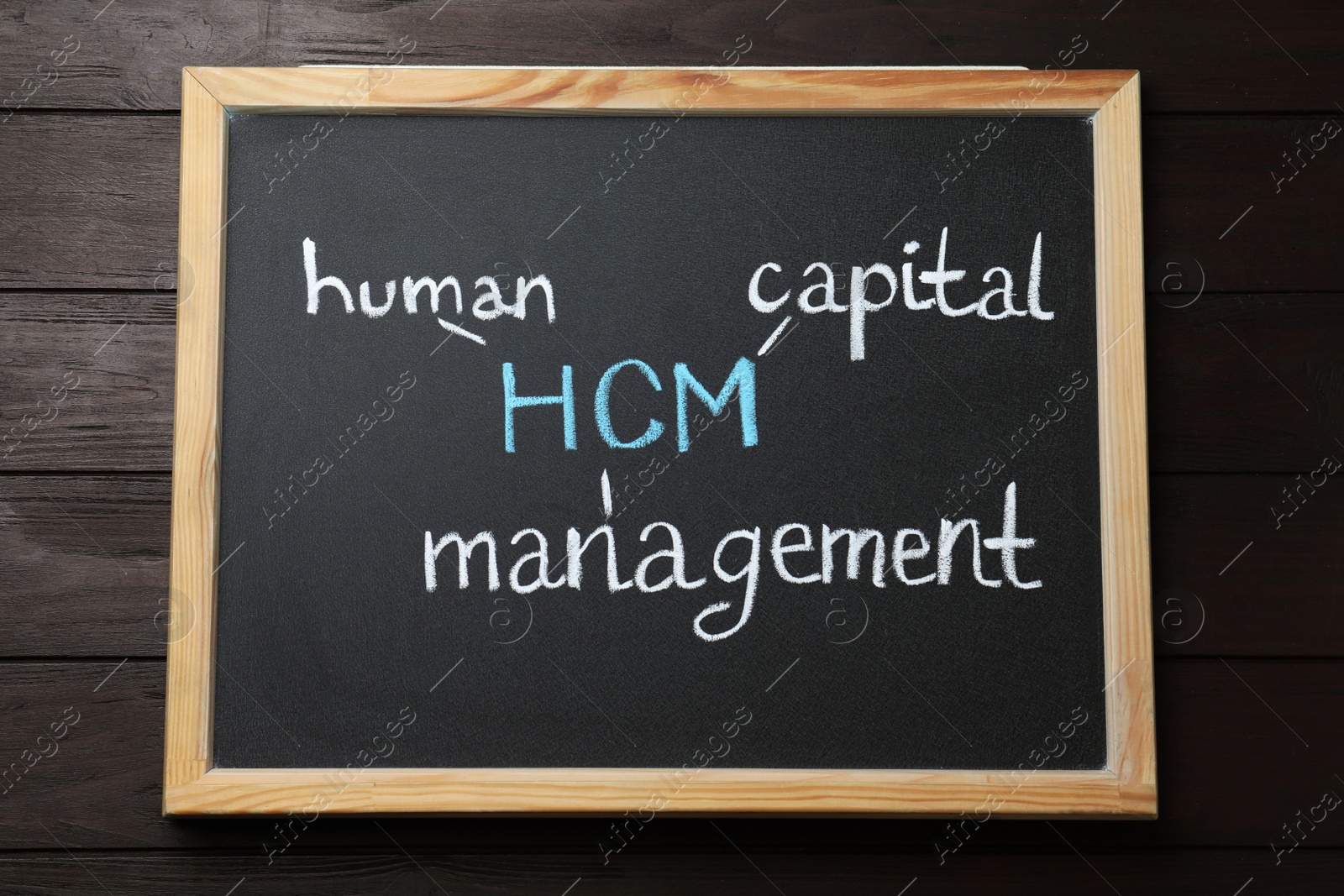Photo of Small blackboard with abbreviation HCM (Human Capital Management) on wooden background, top view