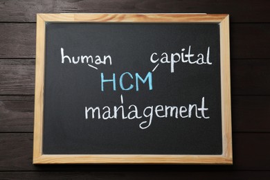 Small blackboard with abbreviation HCM (Human Capital Management) on wooden background, top view