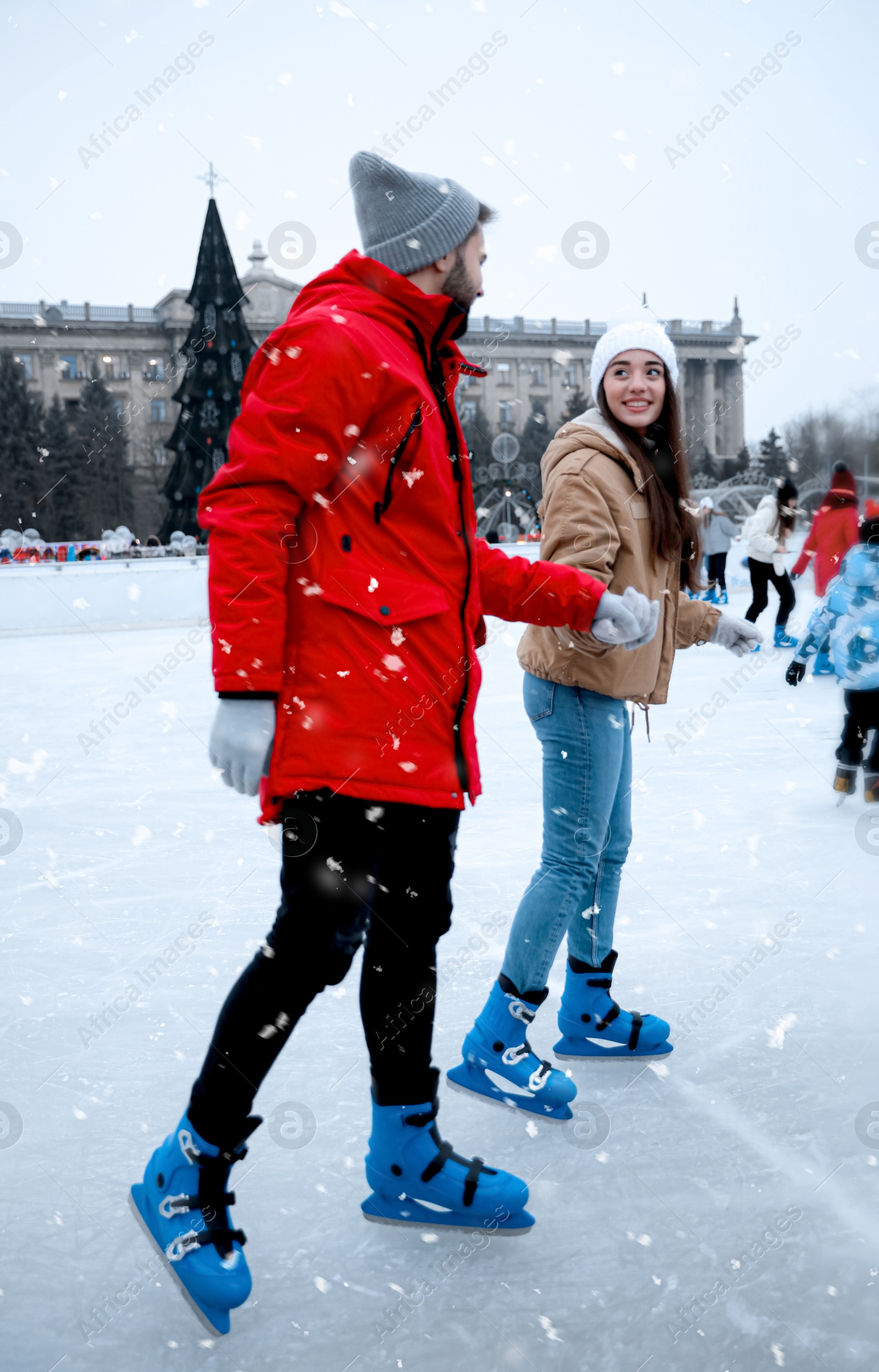 Image of Happy young couple skating at outdoor ice rink