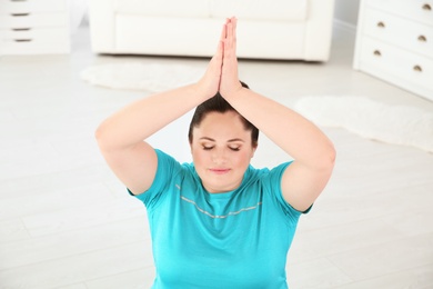Photo of Overweight young woman practicing yoga at home