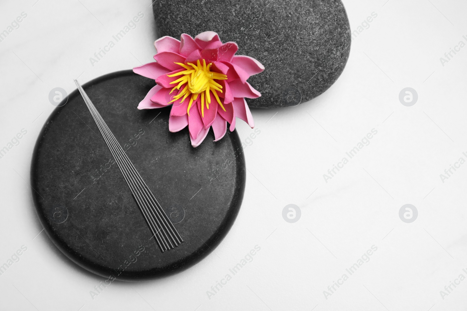 Photo of Acupuncture needles, spa stones and flower on white table, flat lay. Space for text