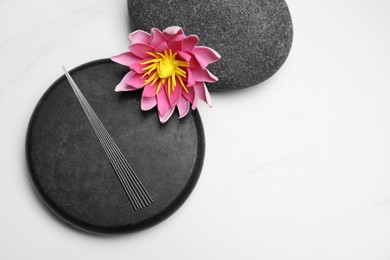 Photo of Acupuncture needles, spa stones and flower on white table, flat lay. Space for text