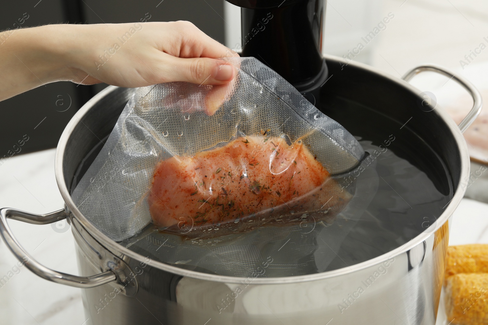 Photo of Woman putting vacuum packed meat into pot with sous vide cooker, closeup. Thermal immersion circulator