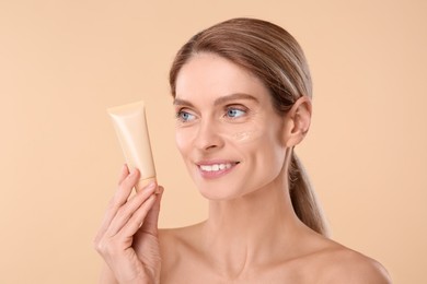 Photo of Woman holding tube of foundation on beige background