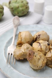 Photo of Delicious pickled artichokes and fork on plate, closeup