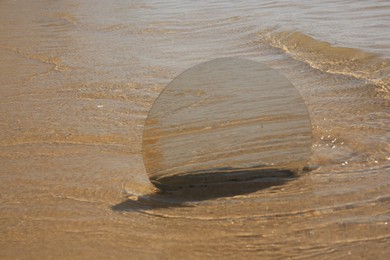 Photo of Round mirror reflecting sea on sandy beach