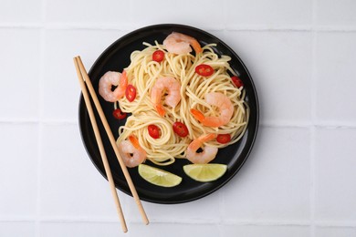 Tasty spaghetti with shrimps, chili pepper and lime on light tiled table, top view