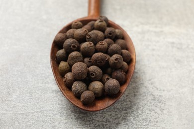Photo of Aromatic allspice pepper grains in wooden spoon on grey table, closeup