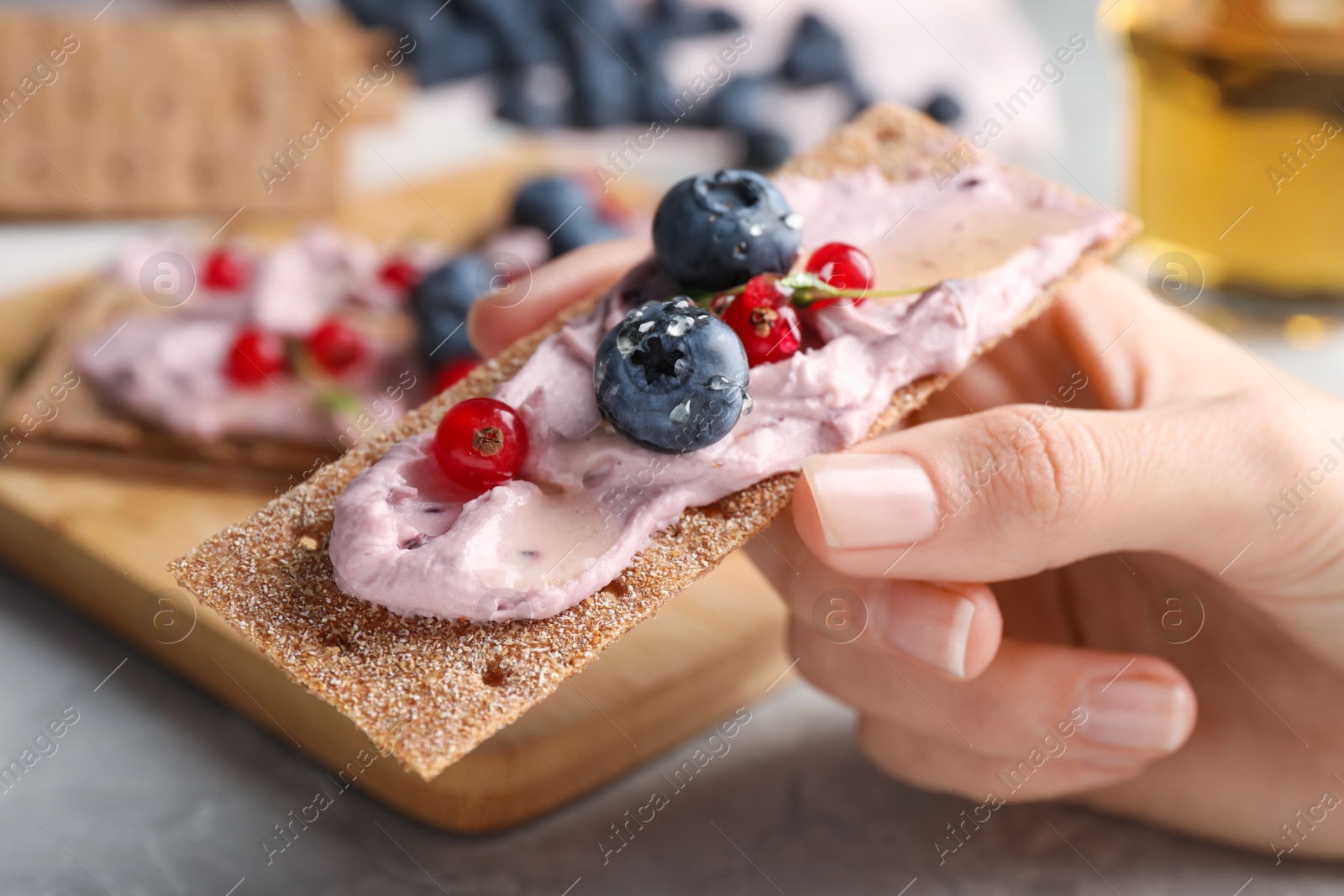 Photo of Woman holding tasty cracker sandwich with cream cheese, blueberries, red currants and thyme at table, closeup